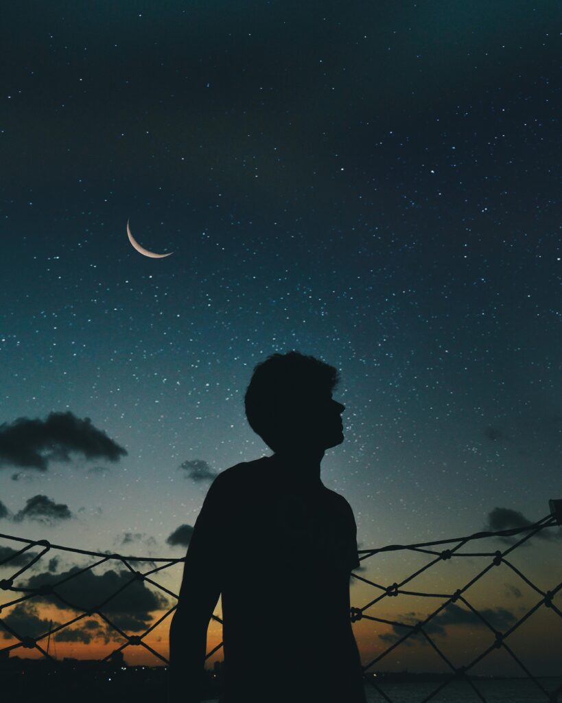pexels-photo-1136575-1136575 A lone silhouette stands beneath a crescent moon and starry sky, evoking a sense of solitude and wonder.